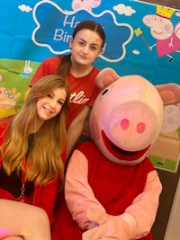 two girls posing with a peppa pig mascot